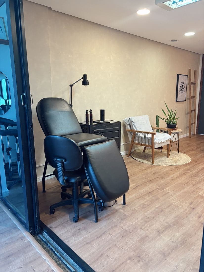 Sala de tatuagem com cadeira preta e poltrona ao fundo